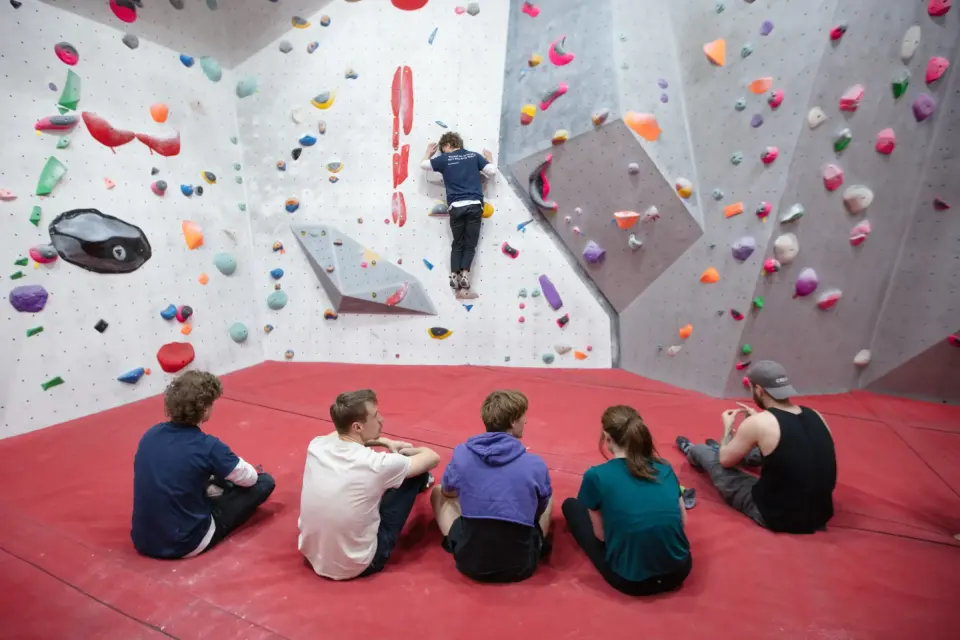 Group on the red matting watching a climber on the bouldering wall