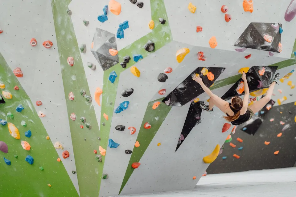 Climber on a grey and green wall covered in colourful holds