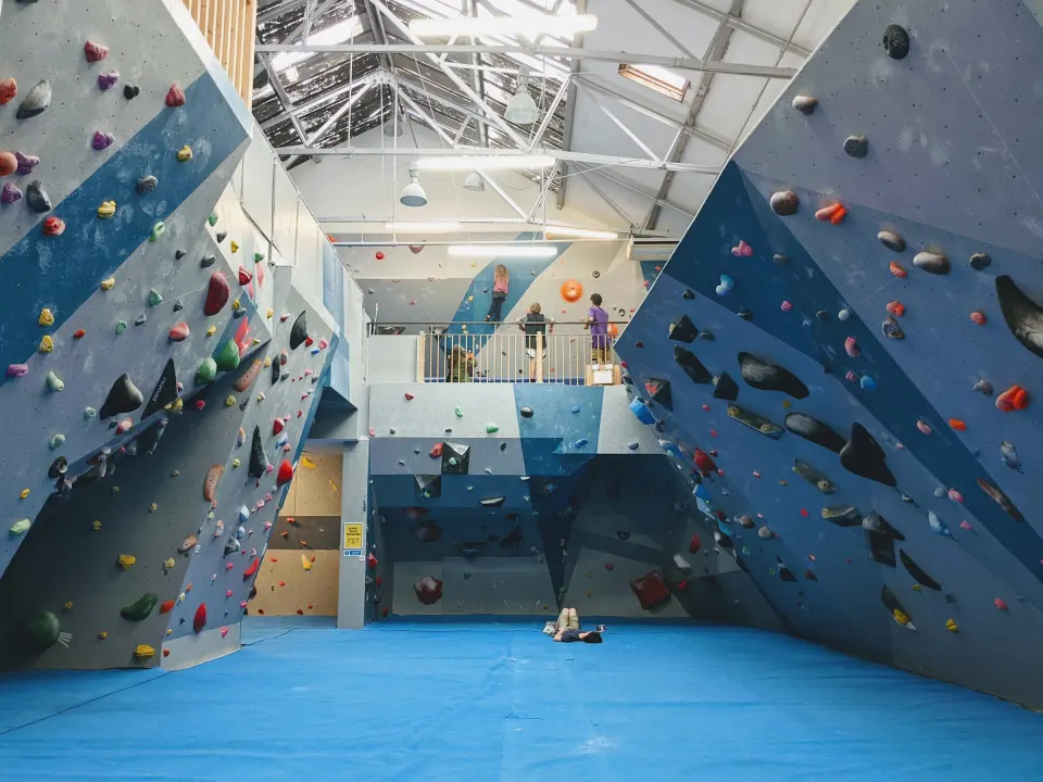 Blue-grey bouldering walls above blue matting under a glass roof
