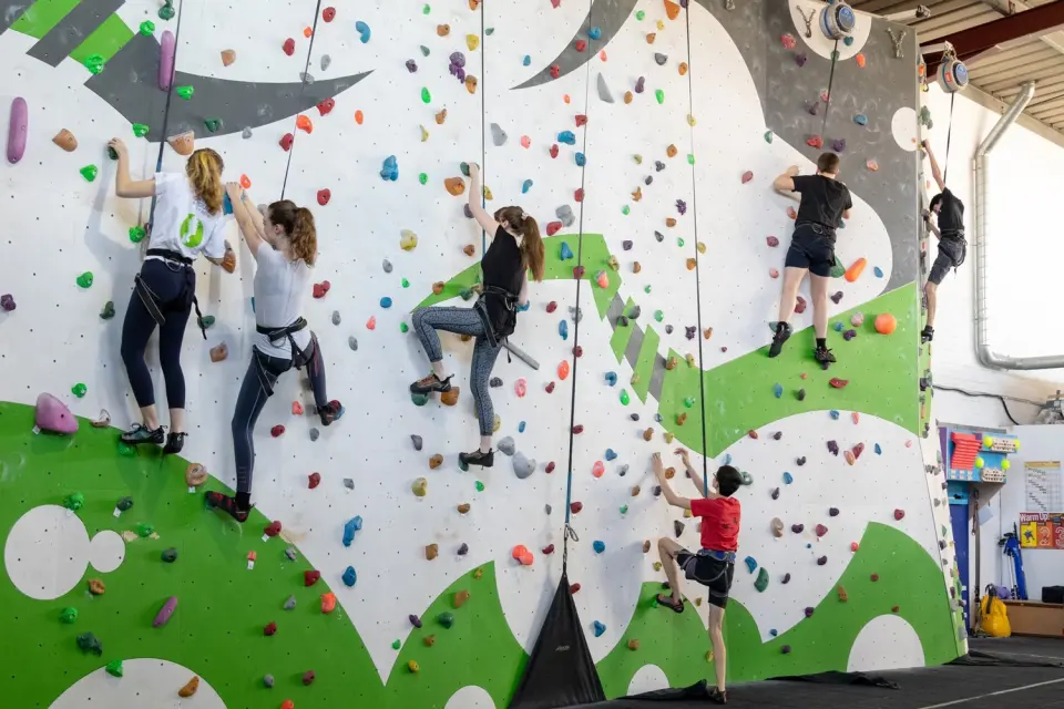 Climbers on top-rope lines across the green and white wall