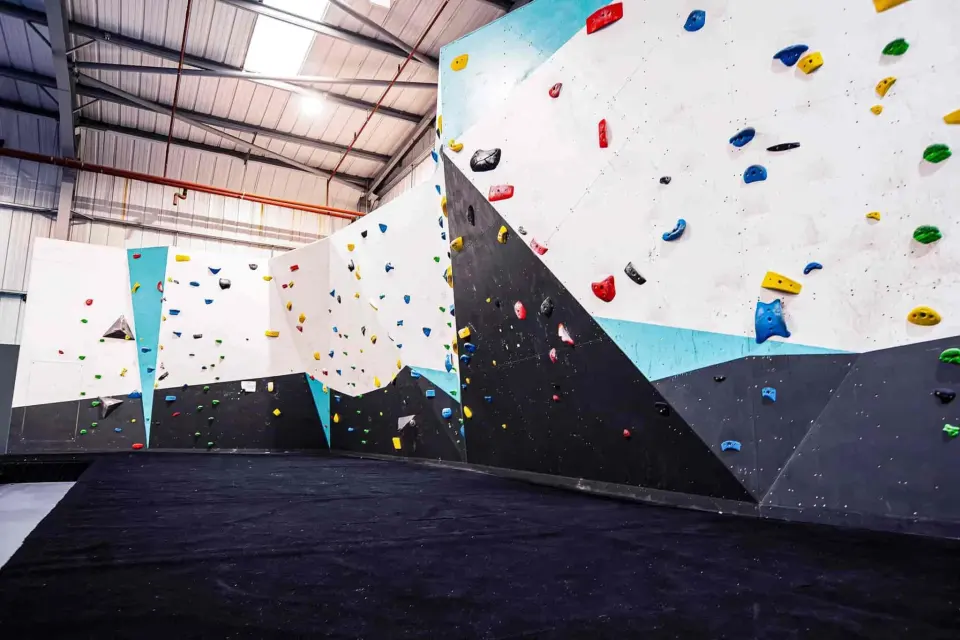 White and teal bouldering wall with black matting below