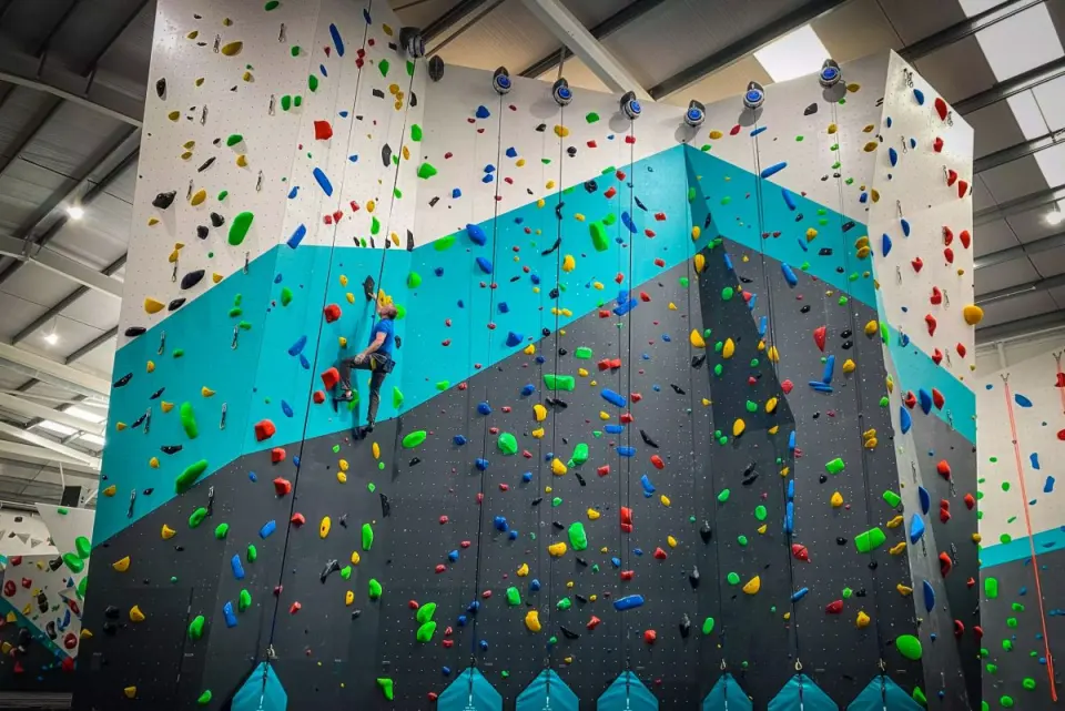 Tall teal and black rope wall with a climber high on the auto-belays