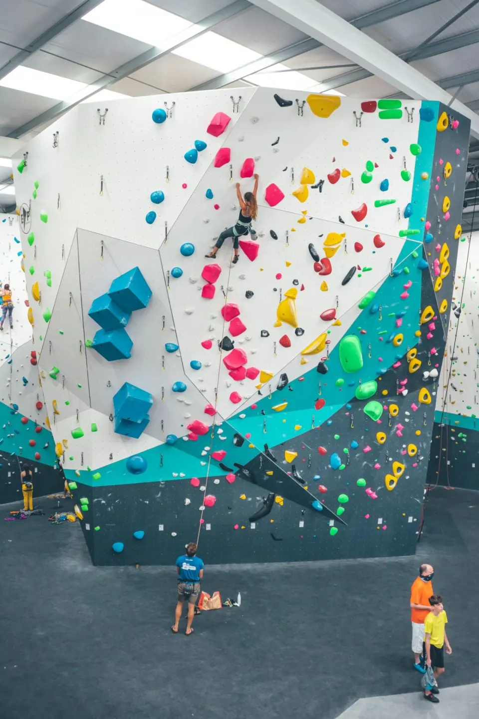 Climber on the tall white and teal competition boulder wall