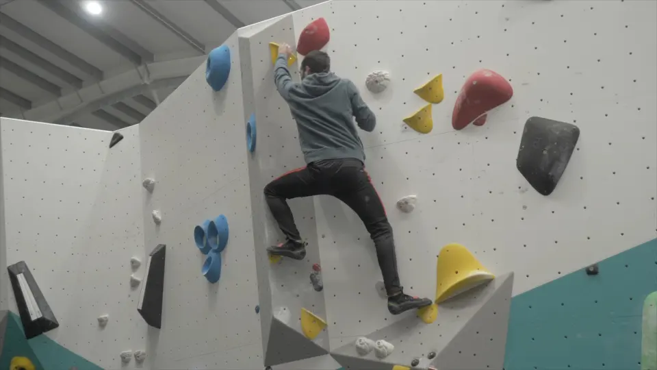 Climber on a white bouldering wall with yellow and blue holds