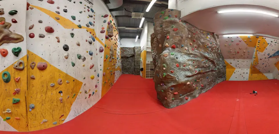 Climbing hall with white and yellow walls, a rock-effect boulder and red matting