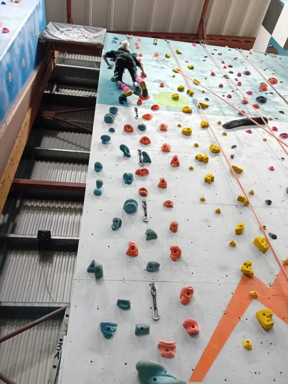 Climber near the top of a grey wall with quickdraws