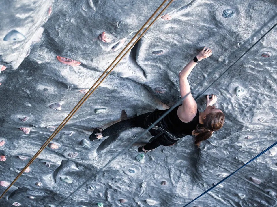 Climber on a grey textured roped wall seen from above