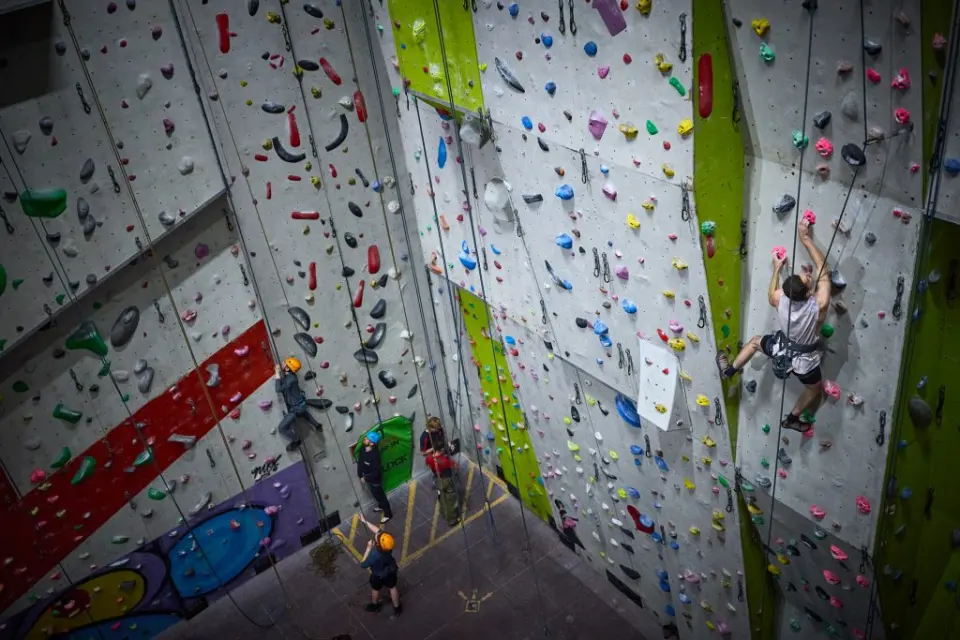 Climbers on tall roped walls with a large red arrow painted on the panels