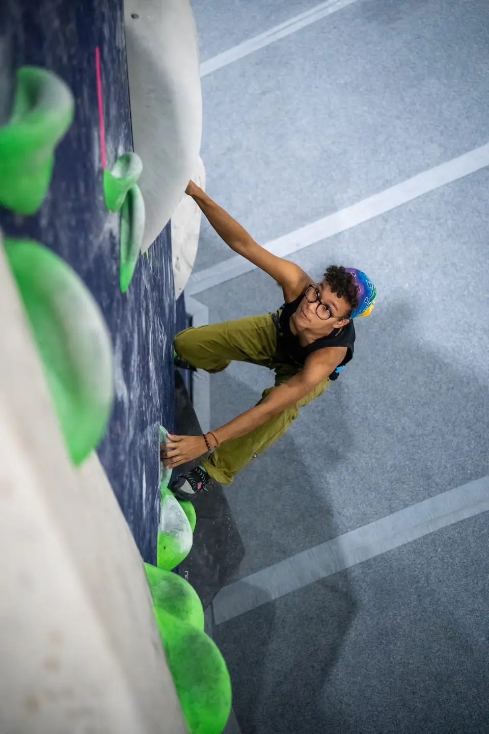 Climber on green holds seen from above the matting