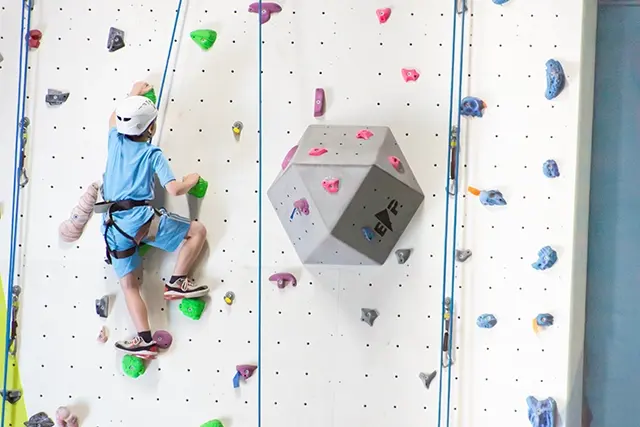 Young climber on a roped line beside a grey volume