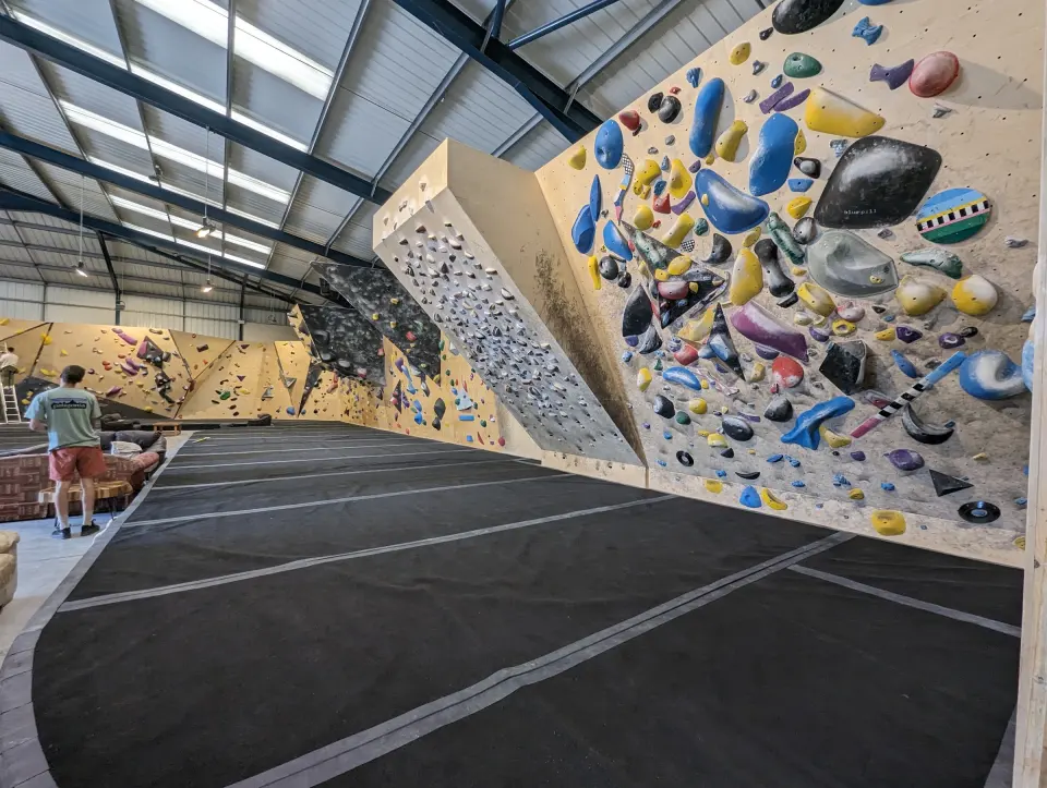 Wooden bouldering walls with colourful holds above black matting