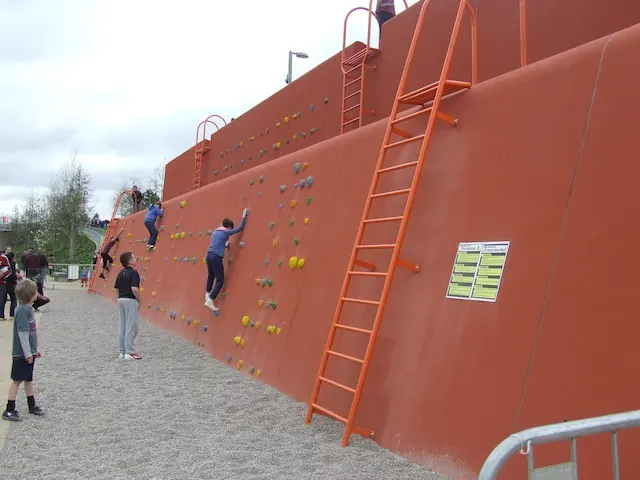 Climbers traversing the long red outdoor wall with ladders