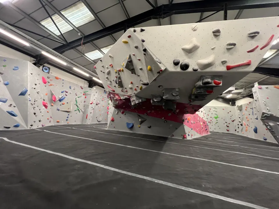 Grey bouldering walls and a large hanging boulder over the matted floor