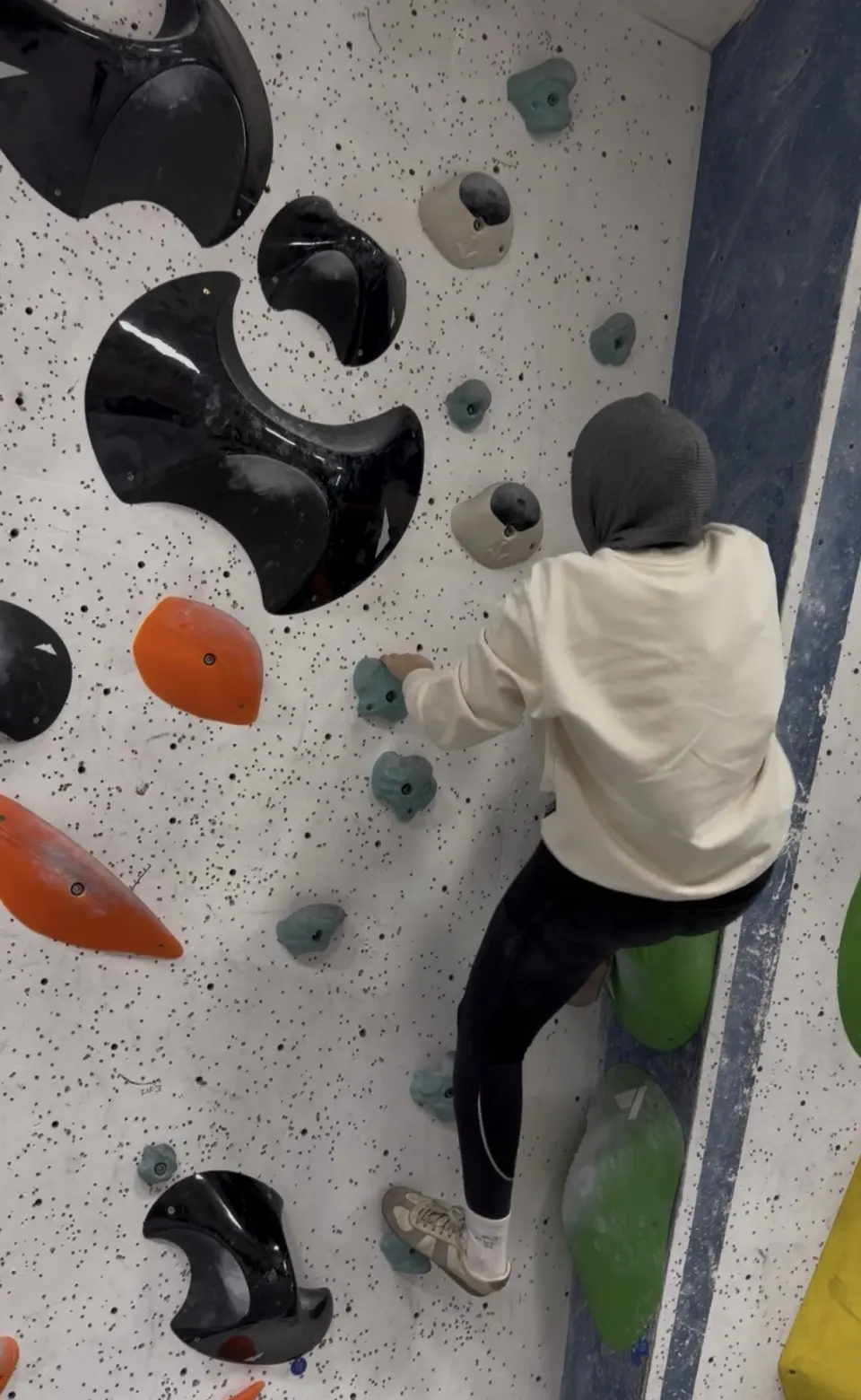 Climber on a speckled white boulder wall with black volumes