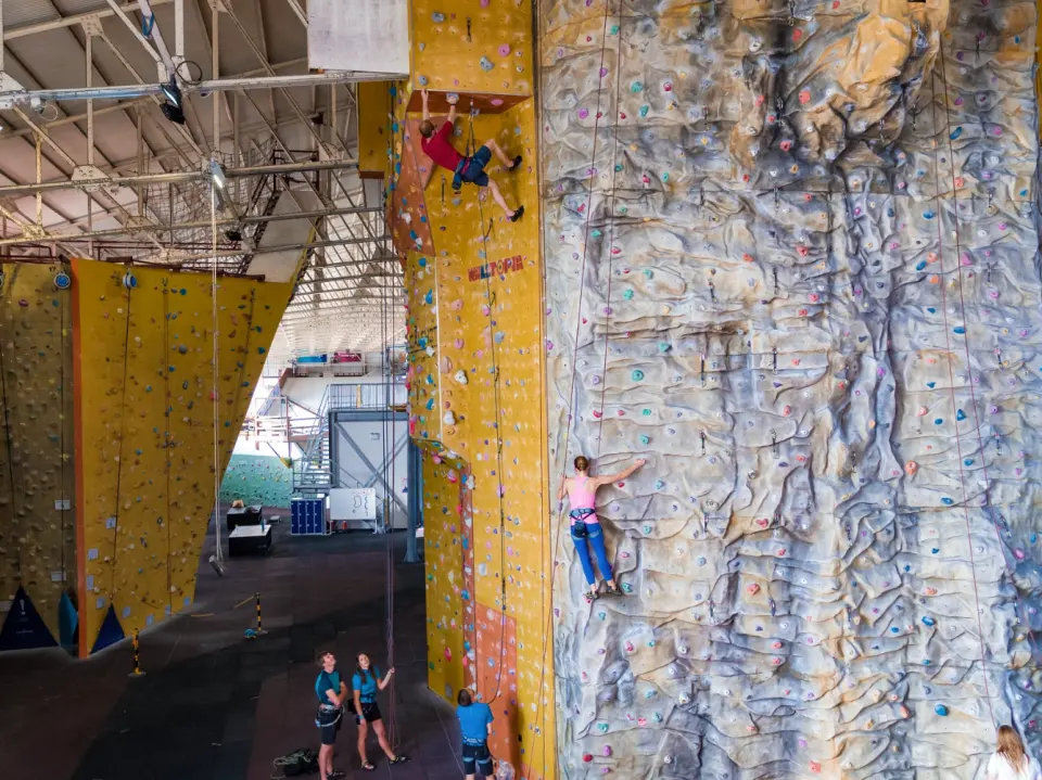 Climbers on the tall yellow and grey roped walls in the hangar