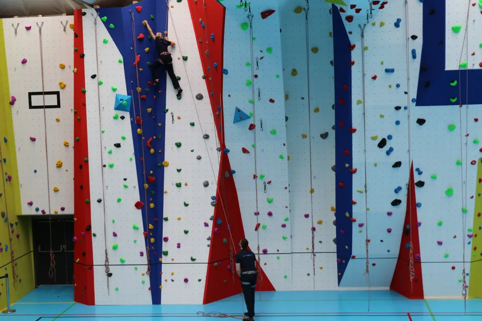 Climbers on the white roped wall with red, blue and yellow panels