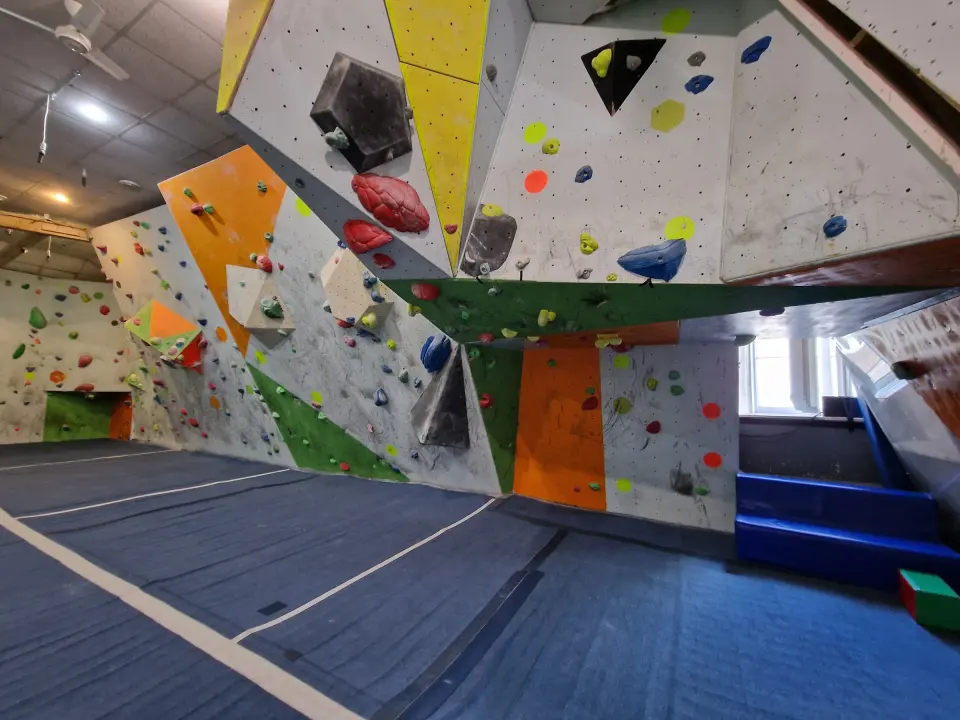 Angled bouldering walls with coloured volumes above blue matting