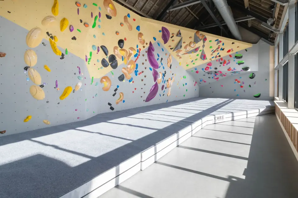 Sunlit bouldering walls with an overhanging yellow roof and grey matting