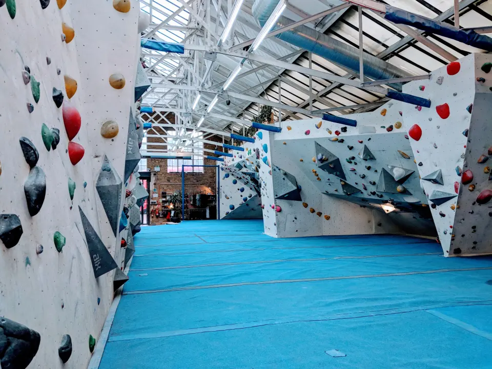 Long bouldering hall with blue matting under a glazed factory roof