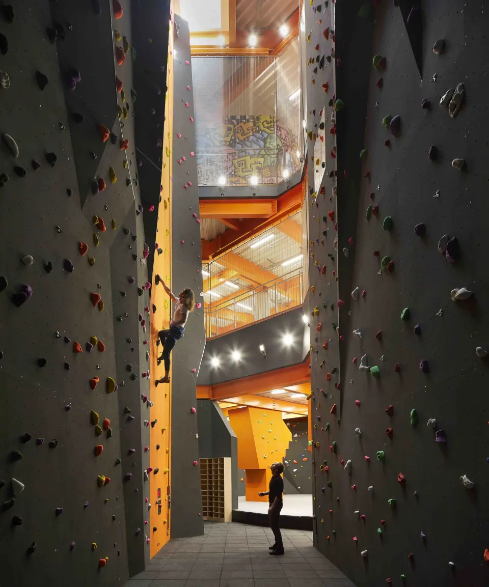 Climber high on the lead walls with the skatepark floors behind
