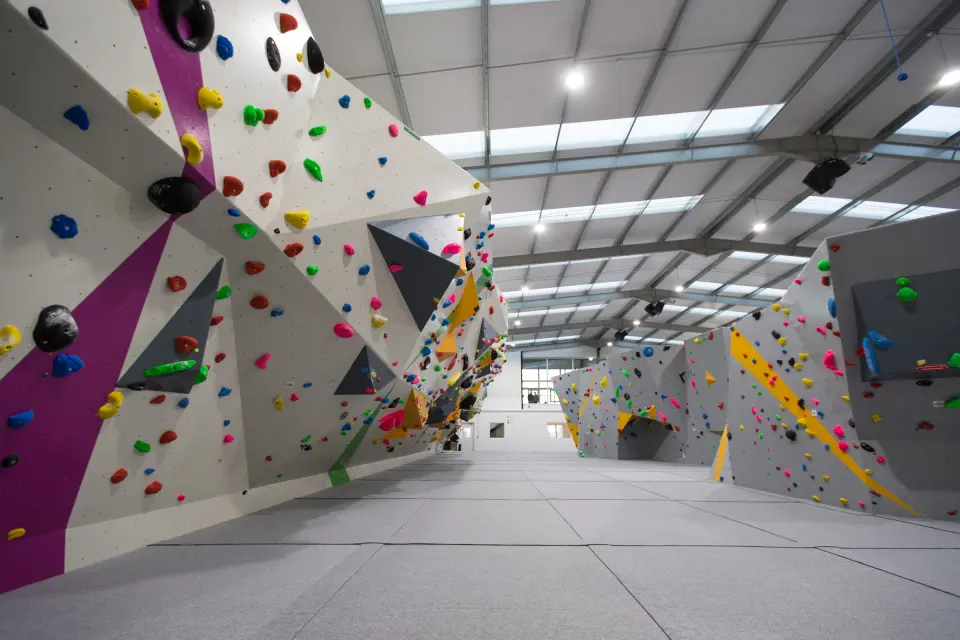 Long grey bouldering wall with colourful volumes under a skylit roof