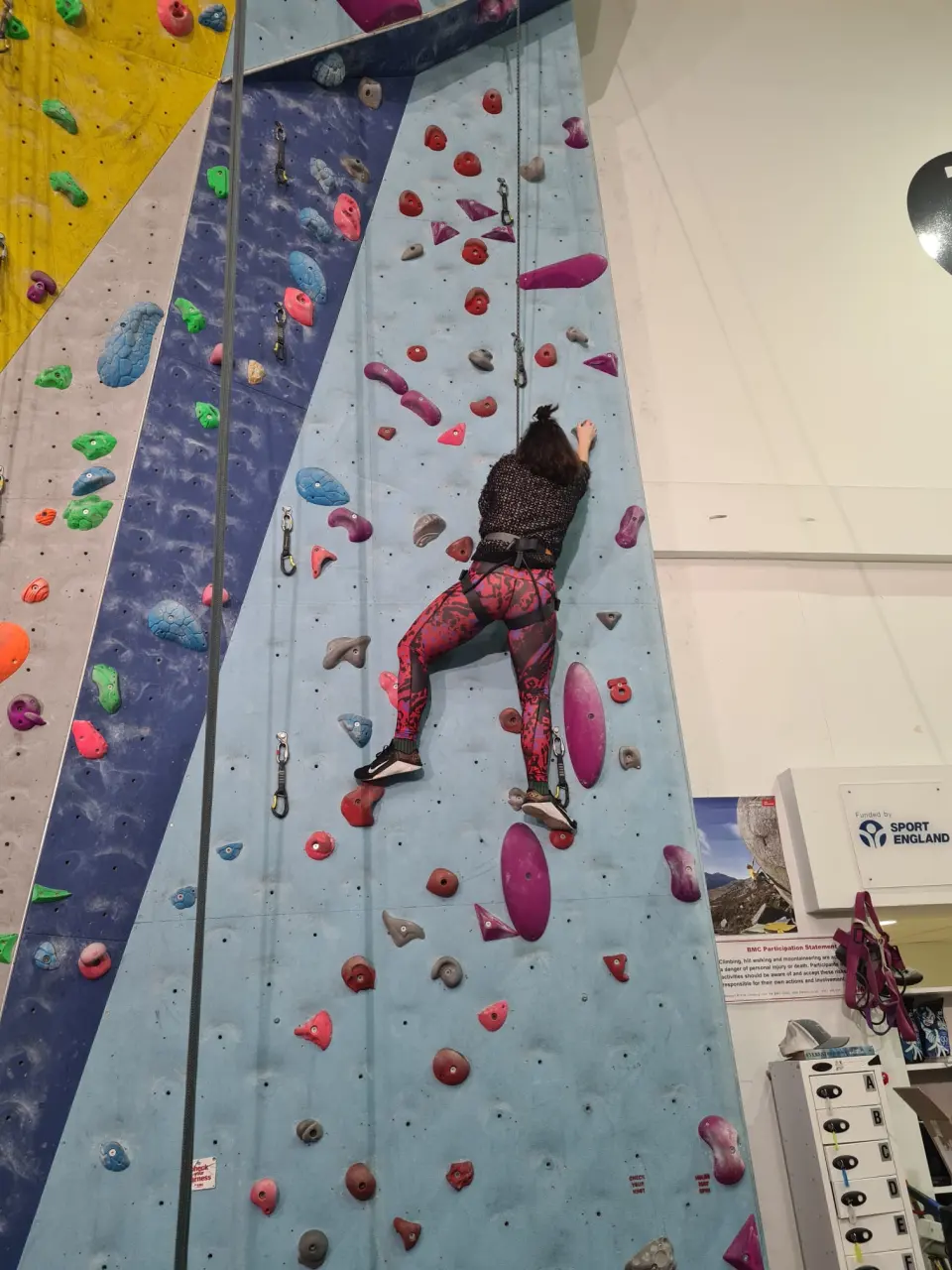 Climber on a blue lead line with pink holds