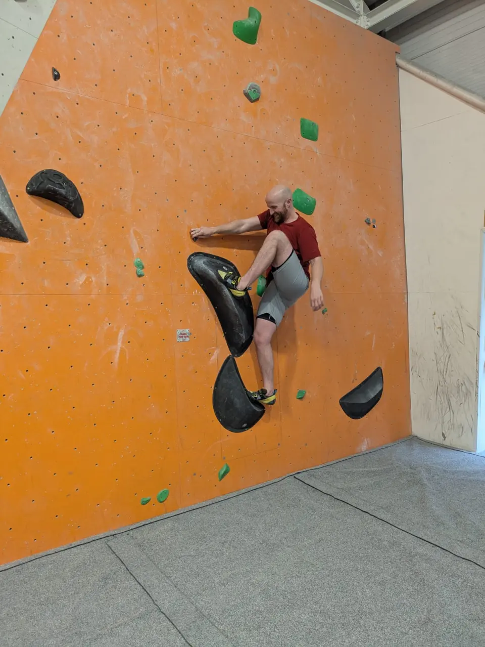 Climber on black volumes on an orange bouldering wall