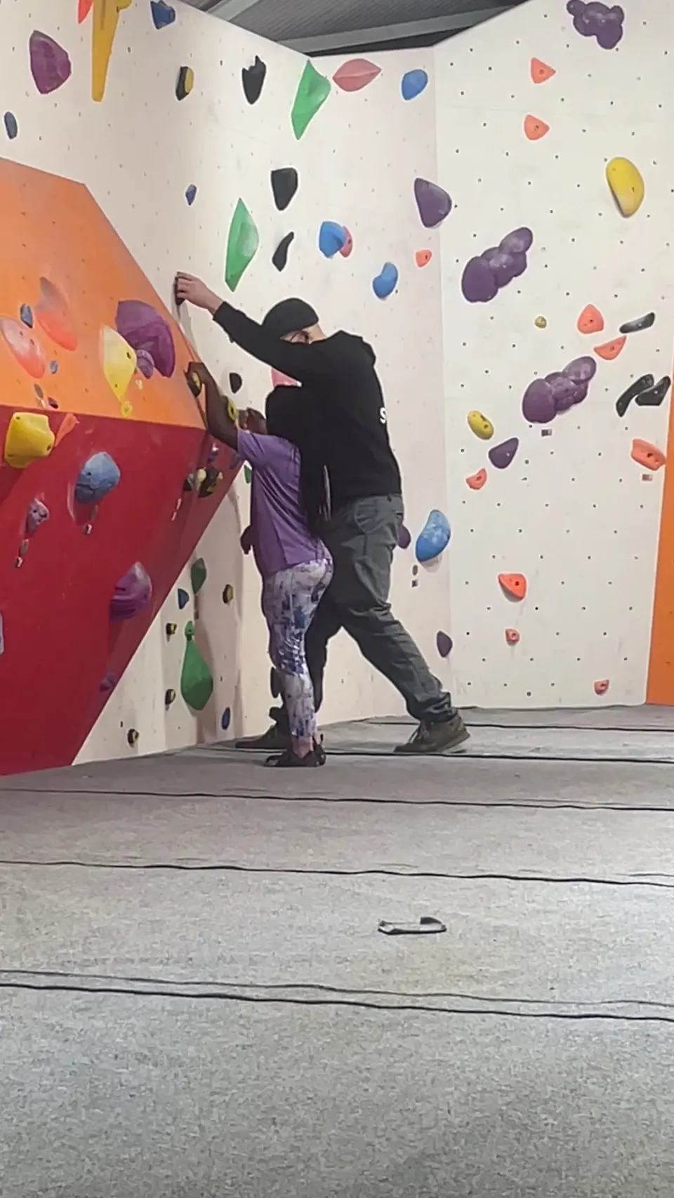 Two climbers on a white and orange bouldering wall