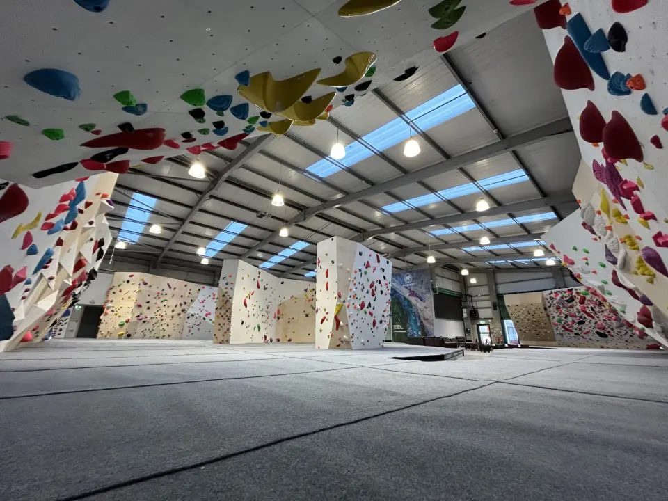 The bouldering hall at BoulderWorld Belfast, with overhanging walls of coloured holds above grey matting