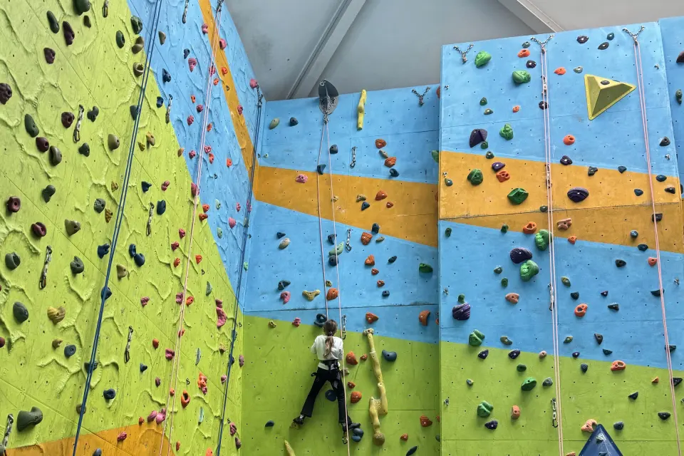 Climber on a top rope on the blue, orange and green 10m wall