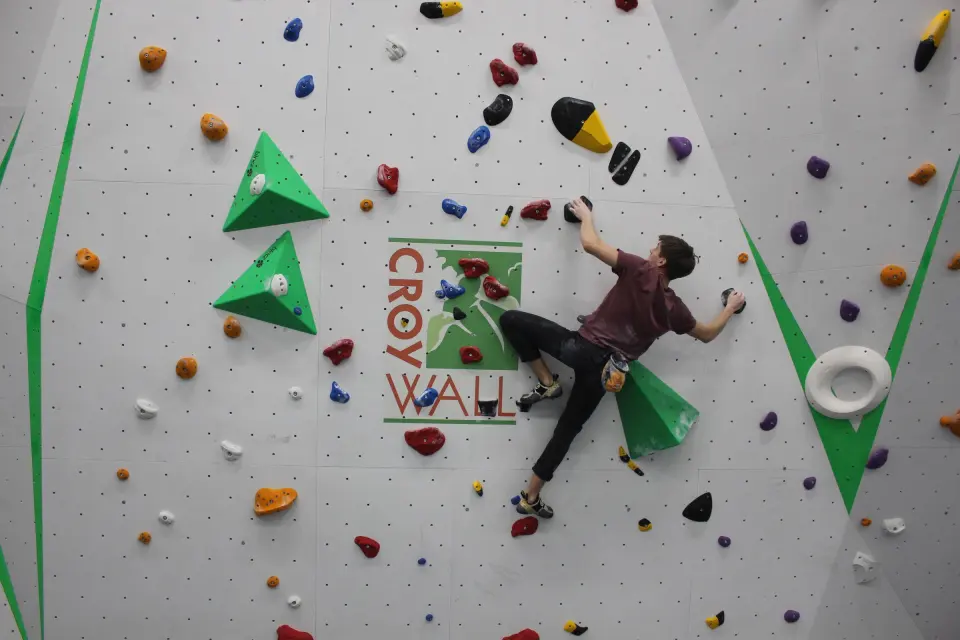 Climber on a wall with green volumes and the CroyWall logo