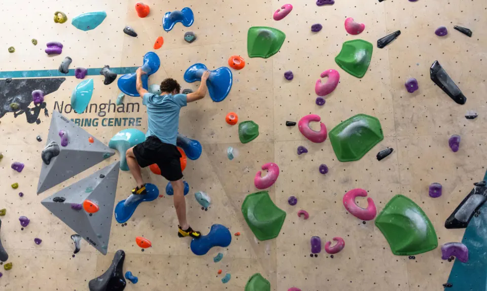 Climber on a wall of green and pink holds by grey volumes