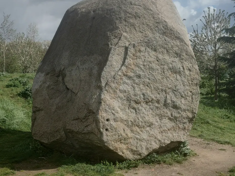 The granite boulder on a grassy mound with trees behind