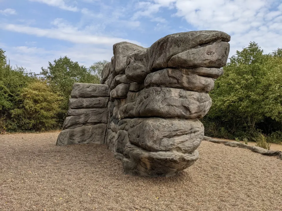 Layered concrete boulder on bark chips with trees behind