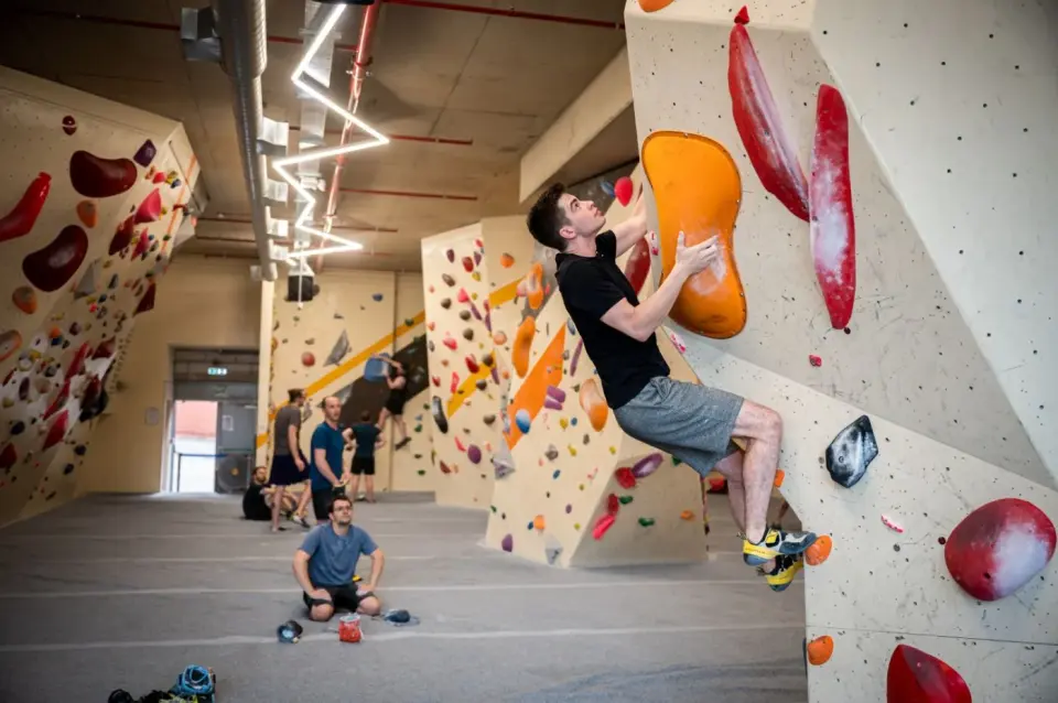 A climber on a steep bouldering wall with large orange and red volumes at Social Climbing Leicester