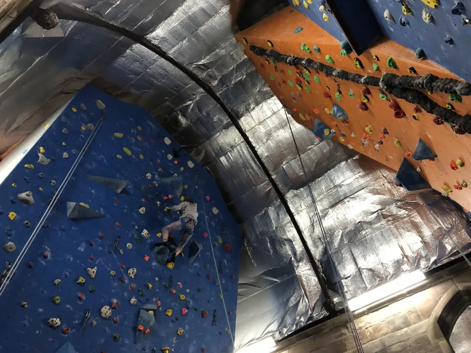 A climber on a blue roped wall beneath the arched roof of Alter Rock in St James Church, Derby