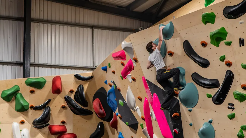 A climber on a steep bouldering wall with large volumes at Brushworks Climbing in Glasgow