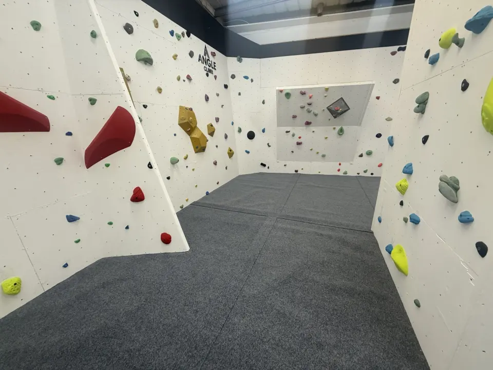 Bouldering walls with coloured holds and volumes over padded flooring at Angle Climb, Peterborough