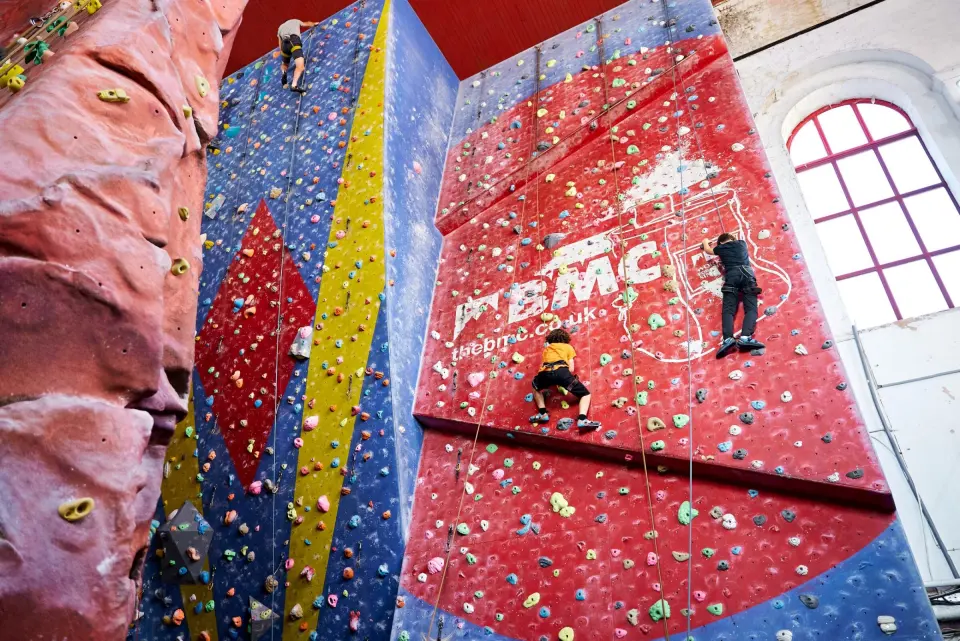 Climbers on the tall red and blue roped walls inside Pear Mill at Awesome Walls Stockport