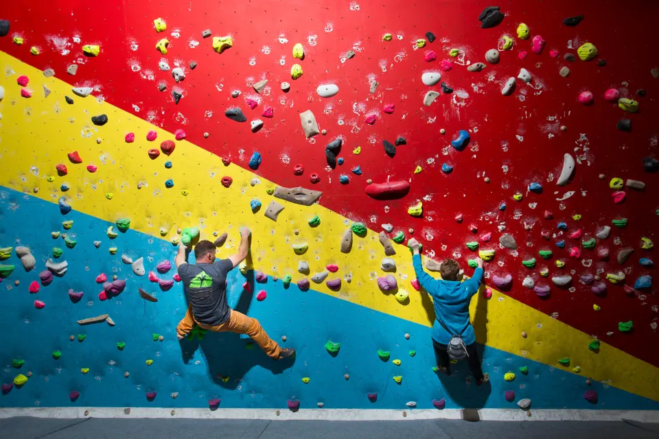 Two climbers on a blue, yellow and red bouldering wall at Eden Rock