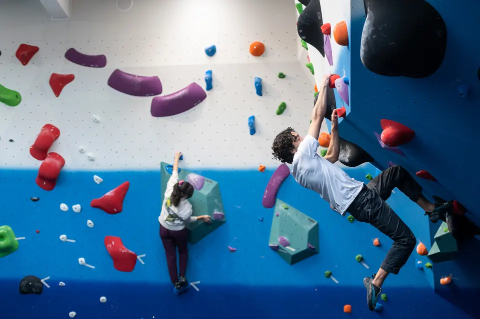Two climbers on a steep blue bouldering wall with red and purple holds at Gallery Bouldering in Oxford