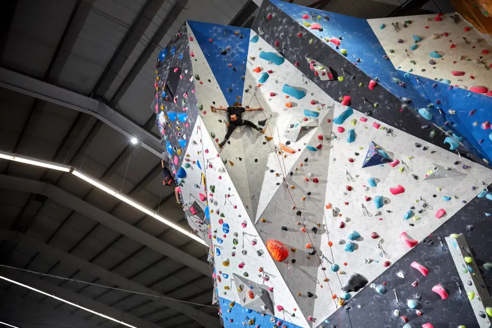 A climber high on the angular white and blue lead walls at High Sports Brighton