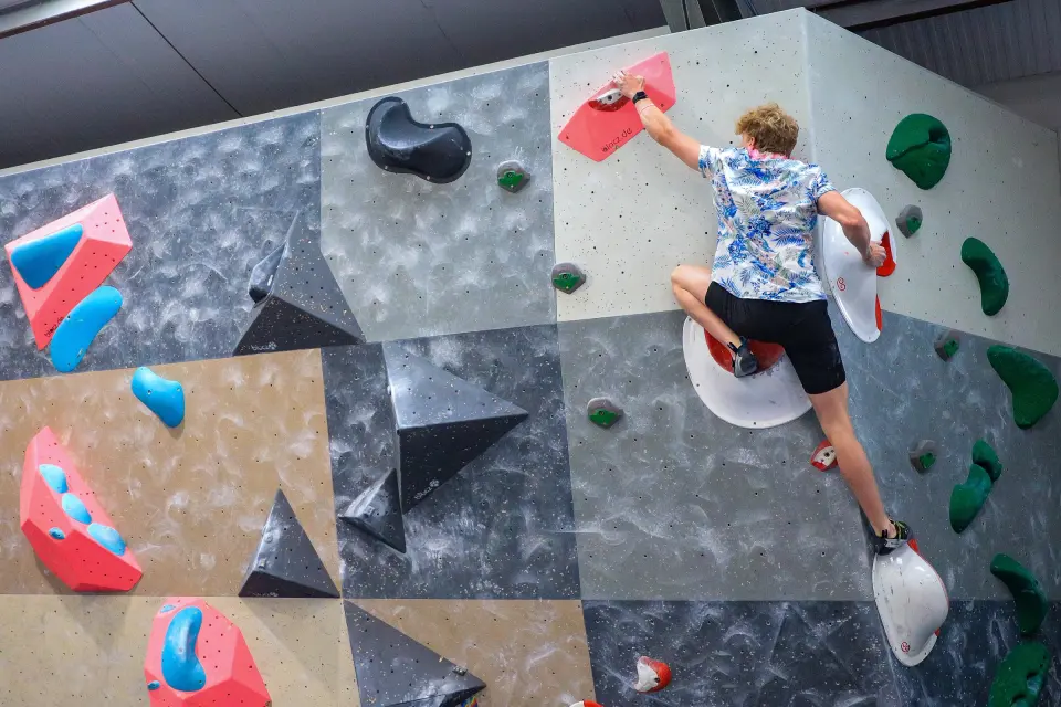 Climber on a grey wall with black and pink volumes