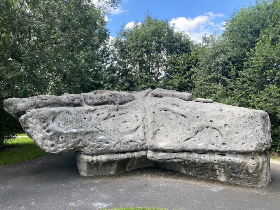 Long grey sculpted boulder covered in pockets beside a path in Heeley Millennium Park