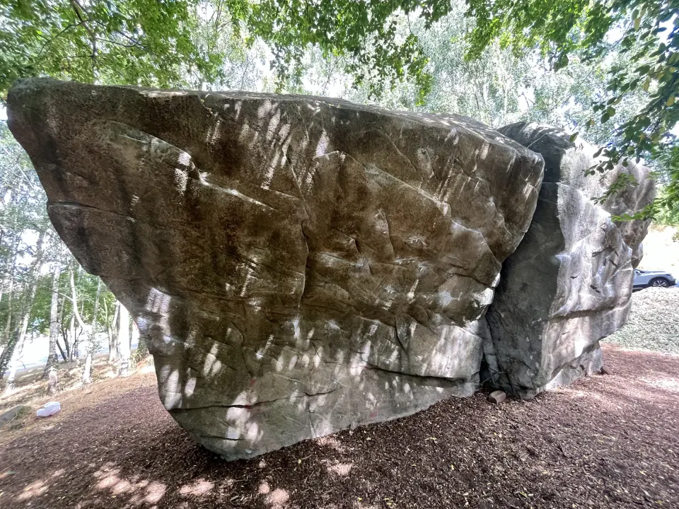 Two leaning sculpted blocks of the Sheaf boulder under trees in Heeley Millennium Park