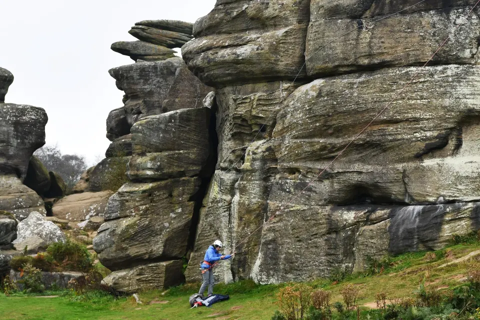 A climber belaying below the gritstone towers of Castle Rocks at Brimham Rocks