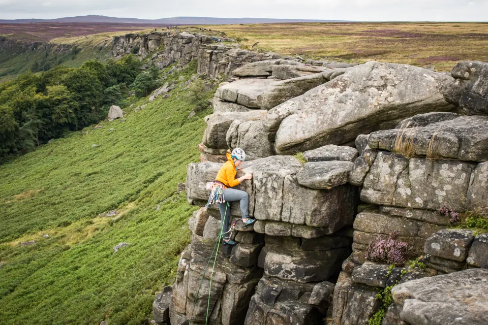 A climber on a gritstone buttress of Stanage Edge, with moorland behind