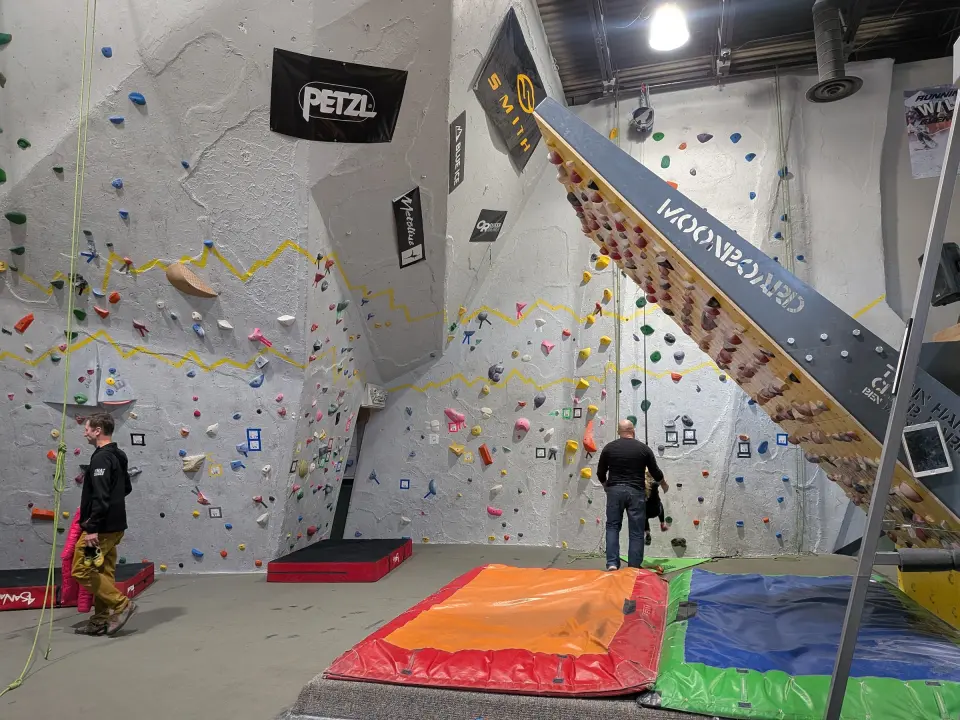 Grey bouldering and roped walls beside the MoonBoard, with crash pads below