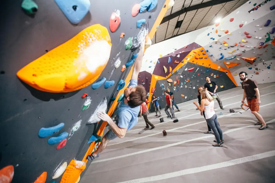 Climber on the overhanging bouldering wall as others watch from the mats
