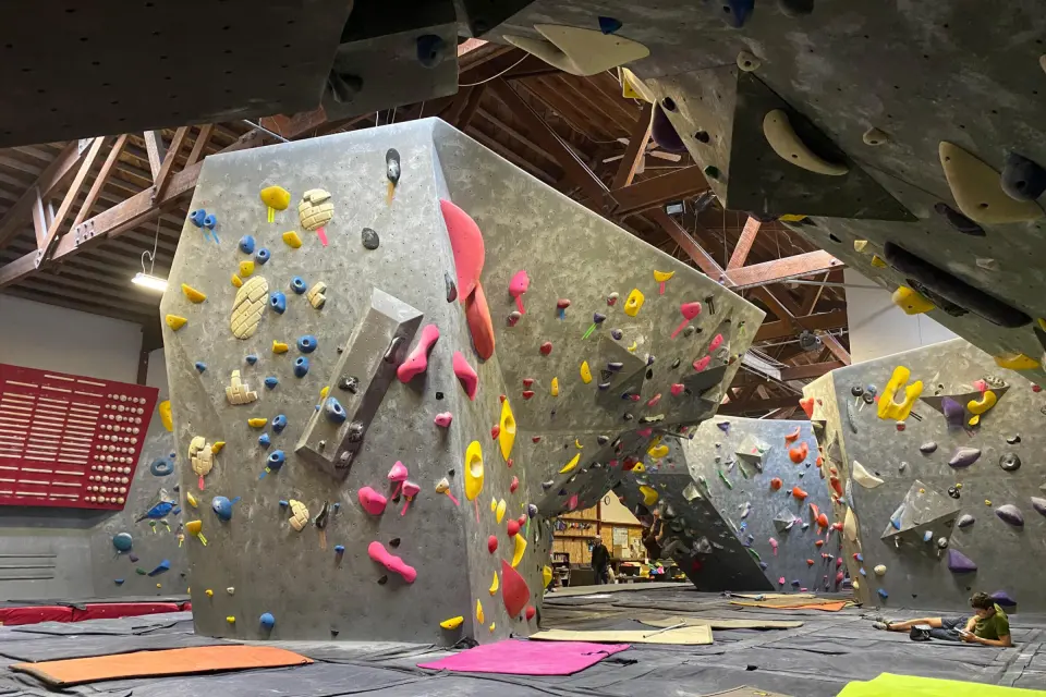 Grey bouldering walls and overhangs under the wooden roof trusses